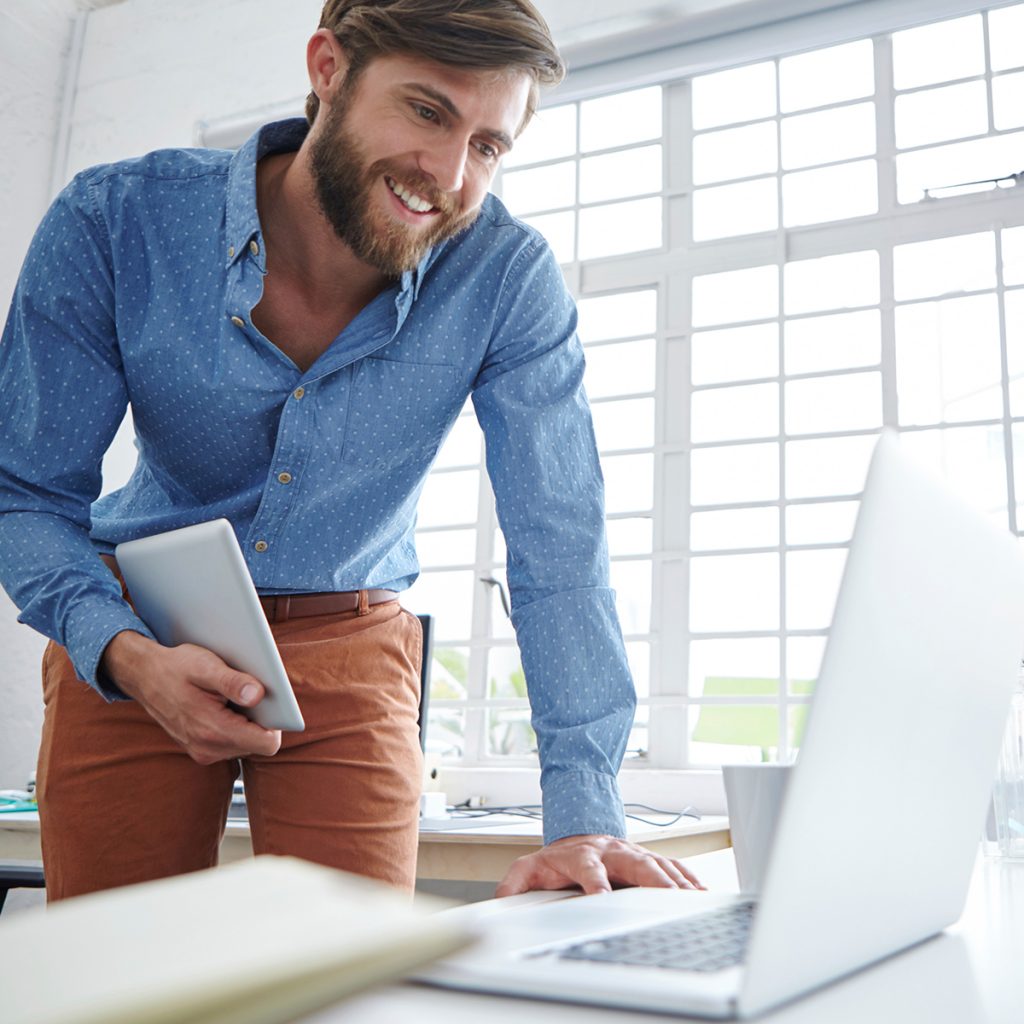 Man-checking-computer-with-tablet-in-hand