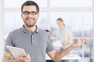 Making your business easy. Cheerful young businessman in casual wear holding digital tablet and smiling while his colleagues communicating on the background